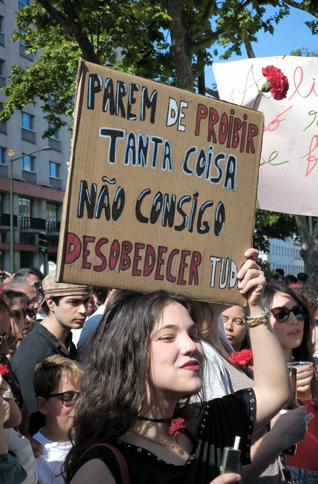 Uma rapariga com ar resolvido e firme, de lábios vermelhos e piercing no nariz, segura um cartaz que diz "Parem de proibir tanta coisa não consigo desobedecer a tudo"